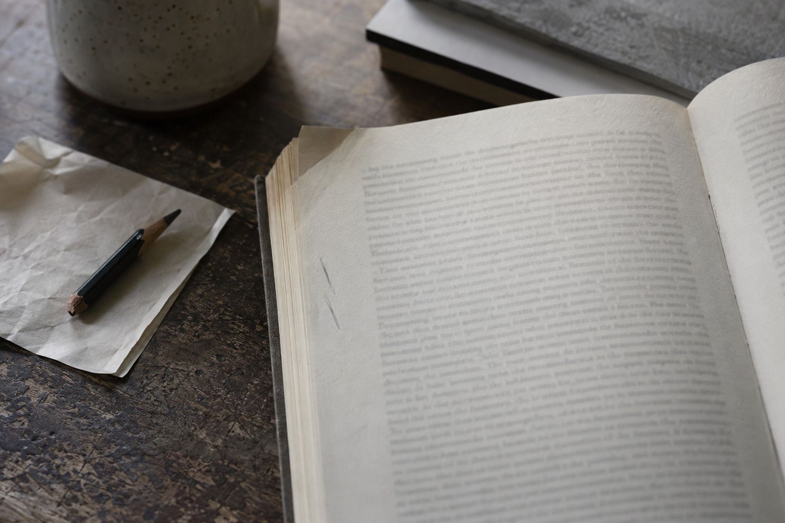 Eine aufgeschlagene Buchseite in Nahaufnahme, der Text ist nicht lesbar. Am linken Rand stehen zwei kurze Bleistiftstriche, das Papier ist an der Ecke leicht gewellt. Daneben liegt ein abgebrochener Bleistift auf einem gefalteten Zettel.